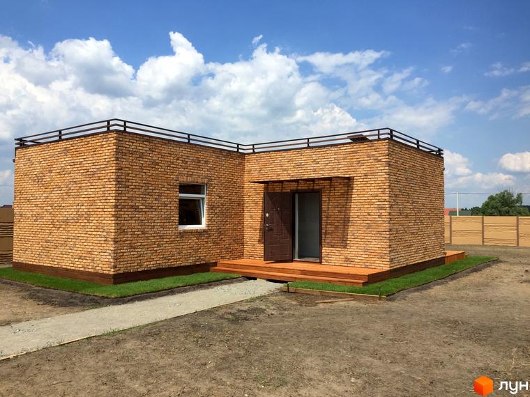 Цегляний будинок з терасою та огородженням на даху. Поруч доглянута прибудинкова територія з газоном та доріжкою.