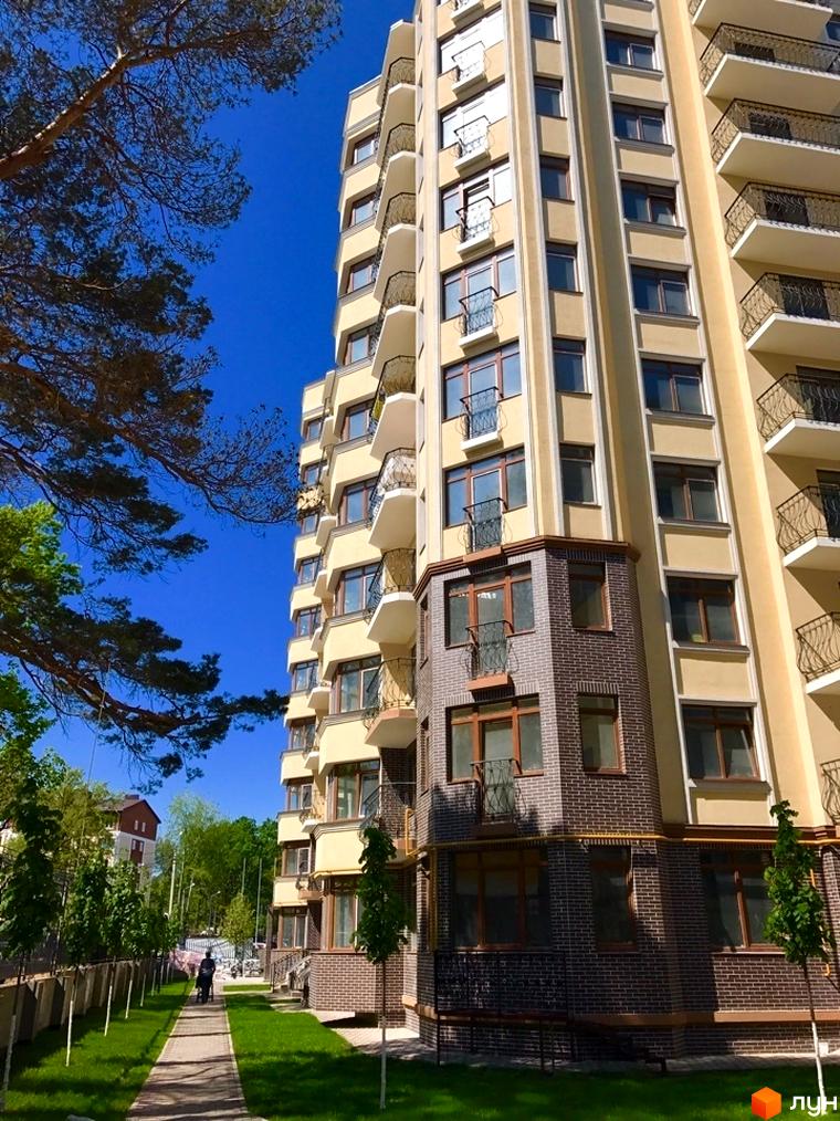 Житловий комплекс Rich Town з жовтим фасадом та балконами з кованими решітками. Поруч доглянута прибудинкова територія з газоном та деревами.