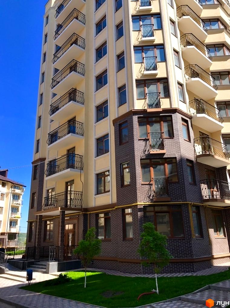 Фасад новобудови ЖК Rich Town з балконами та вікнами. Прибудинкова територія з газоном та тротуаром.