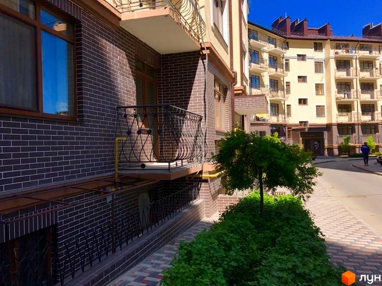 Житловий комплекс Rich Town: фасади будівель з темної цегли та світлої штукатурки, балкони з кованими огорожами, зелена прибудинкова територія з деревами та кущами.