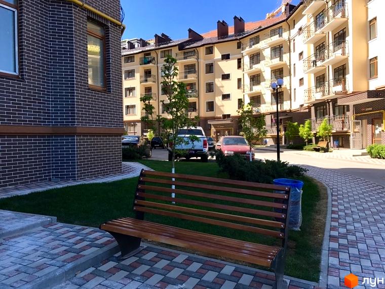 Житловий комплекс Rich Town з цегляними фасадами та доглянутою прибудинковою територією з лавками та зеленими насадженнями. На території комплексу розташовані автомобілі та ліхтарний стовп.