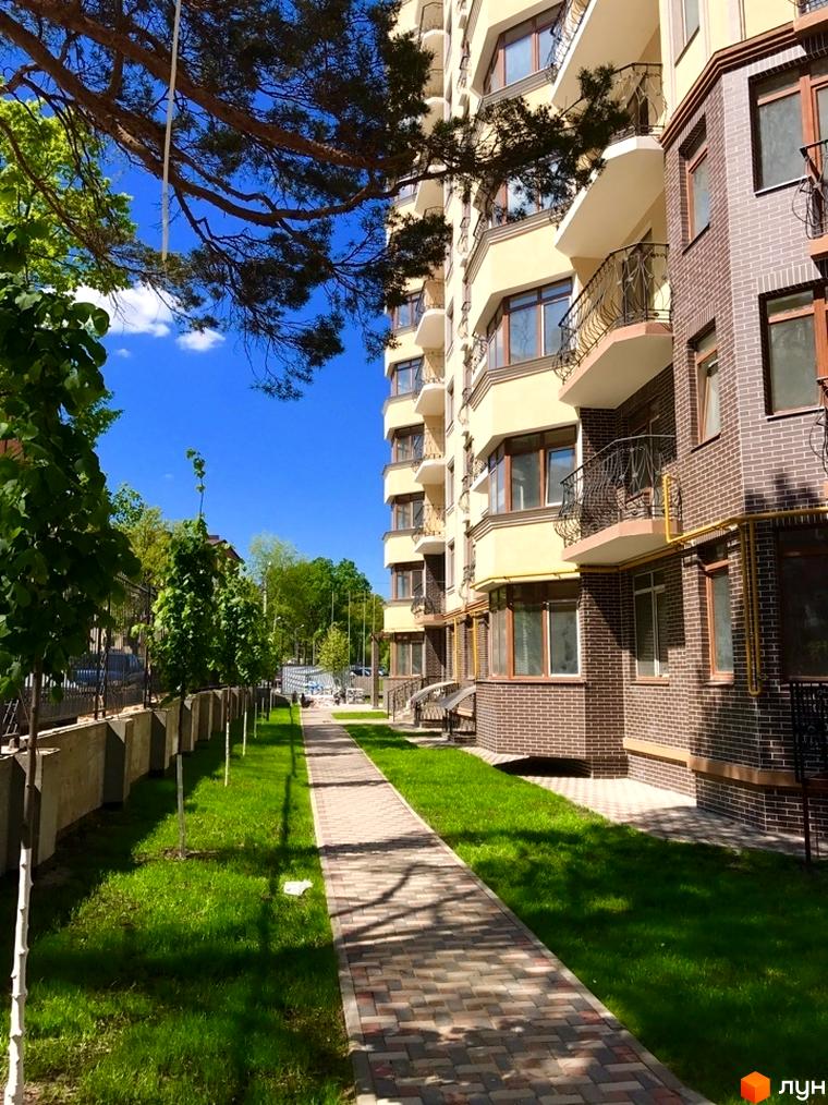 Житловий комплекс Rich Town: світлий фасад, цегляна обробка, балкони з кованими елементами. Доглянута прибудинкова територія з зеленою травою та доріжками.