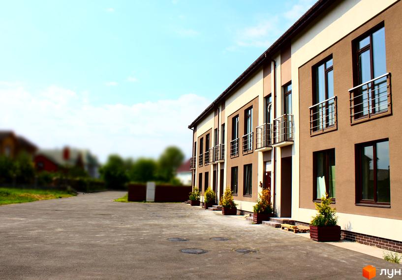 Таунхаус „Деснянська садиба“: будівля з коричнево-бежевим фасадом та балконами. Перед будинком розташований асфальтований майданчик.