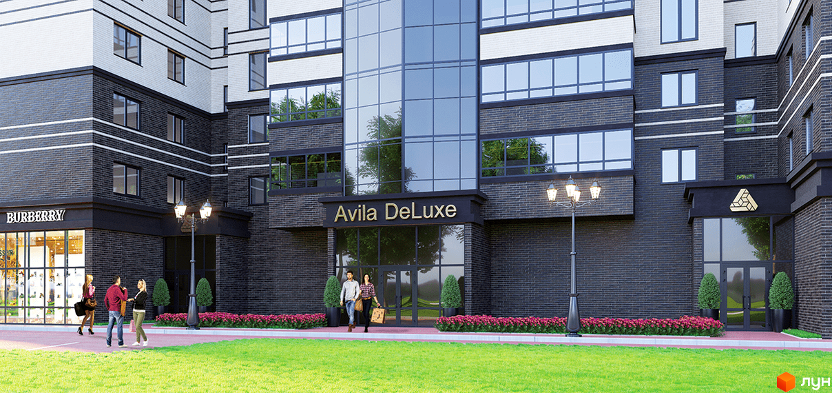 Житловий комплекс Avila DeLuxe з фасадом з темної цегли, білими смугами та скляним входом. Навколо будинку зелений газон, доріжки та клумби.