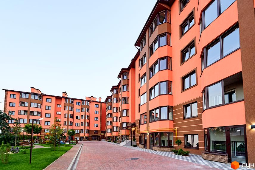 Житловий комплекс Волошковий. Фасад будинку в персикових тонах з коричневими елементами, панорамними вікнами. Зелена прибудинкова територія з дитячим майданчиком та зонами відпочинку.