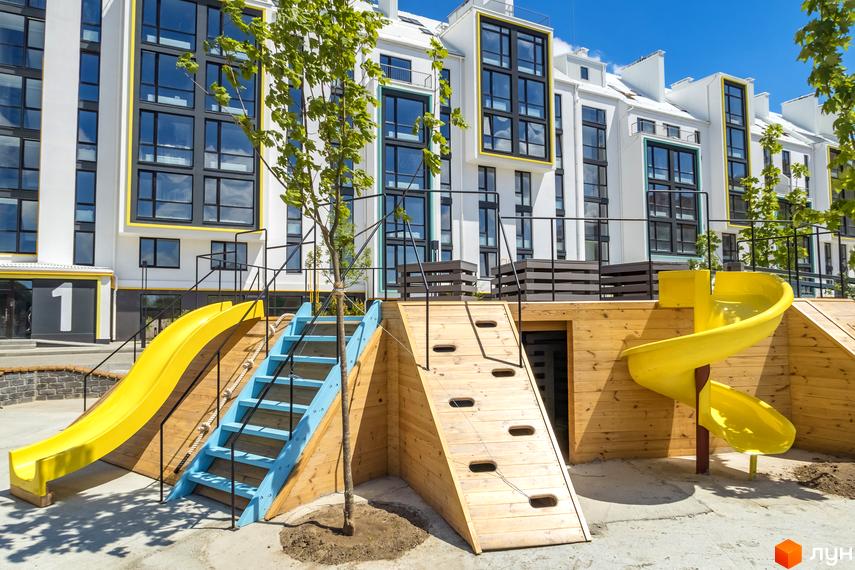 Житловий комплекс City Lake з білим фасадом та великими вікнами. На передньому плані дитячий майданчик з гірками та сходами.