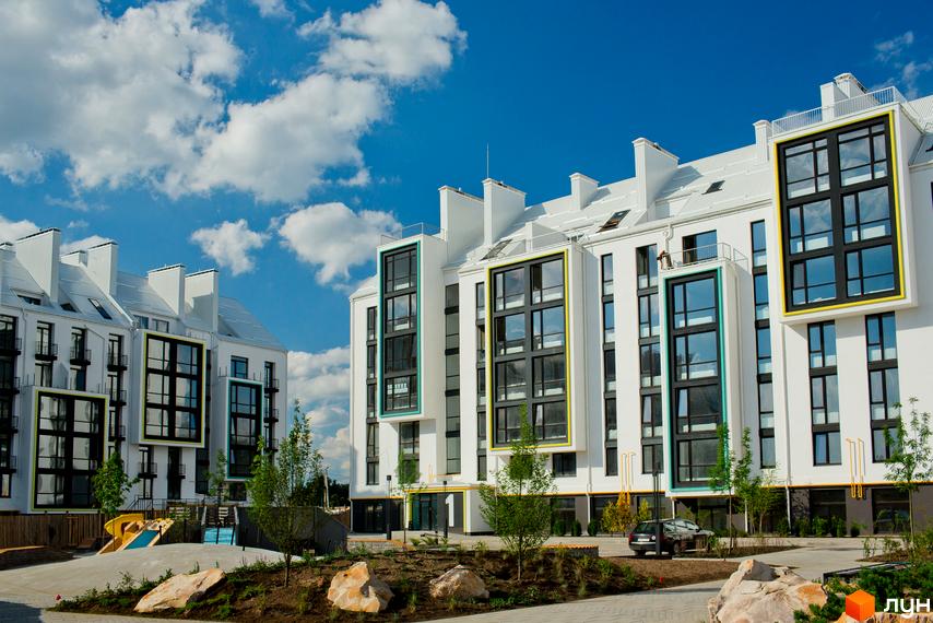 Житловий комплекс City Lake: білі будинки з великими вікнами та кольоровими рамами. Прибудинкова територія з деревами, камінням та дитячим майданчиком.