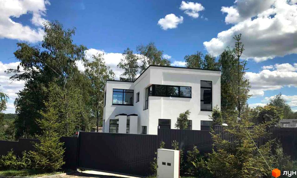 Білий двоповерховий будинок з чорними вікнами в Котеджному містечку Barberry Park. Навколо будинку зелені дерева та паркан.