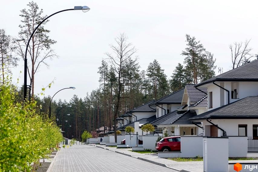 Котеджне містечко КМ Belgravia: сучасні білі будинки з темними дахами та доглянутою прибудинковою територією з бруківкою та зеленими насадженнями.