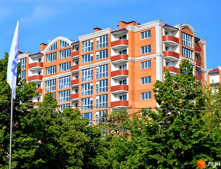 Новобудова на вулиці Шевченка, 99а, 99б, 101а. Багатоповерховий будинок з червоної цегли з білими декоративними елементами та червоними балконами на тлі блакитного неба та зелених дерев.