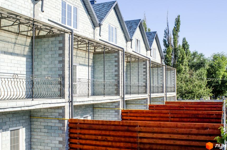 Зображення таунхаусів у Житловому районі „На Байкальській“. Вигляд на фасади будинків з балконами та огорожею, а також дерева на задньому плані.