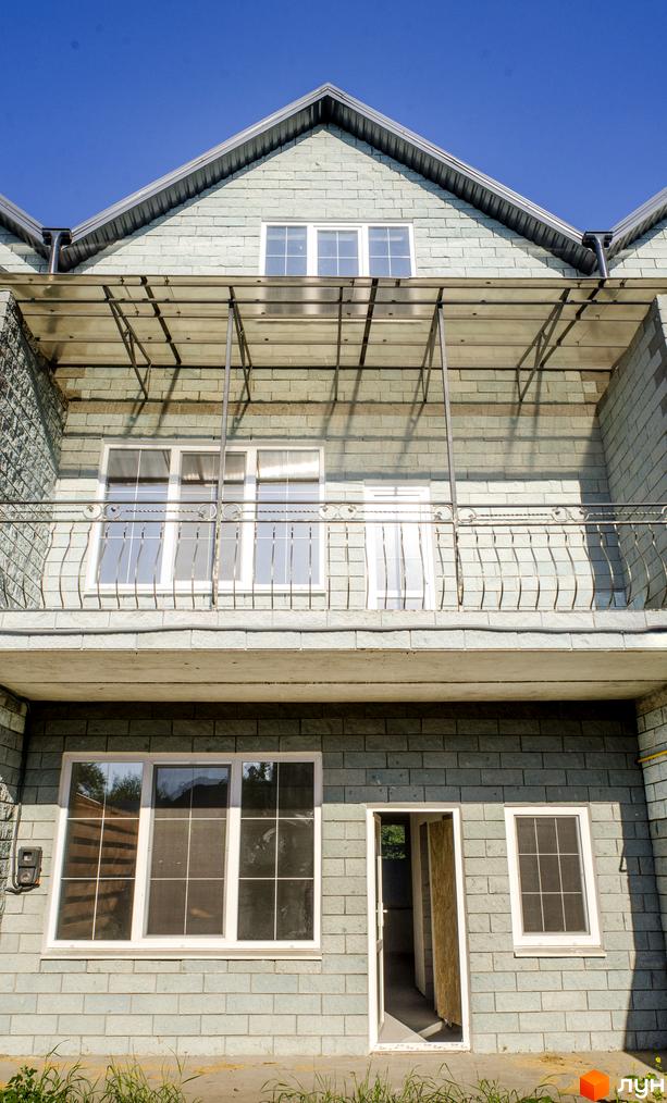 Зображення будинку в Житловому комплексі „На Байкальській“. Двоповерховий будинок з балконом та великими вікнами, збудований з цегли світлого кольору.