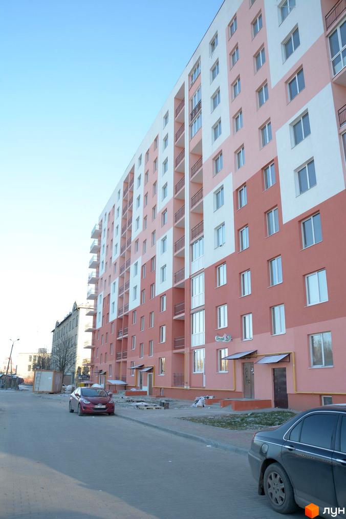 Зовнішній вигляд багатоповерхового будинку Житлового комплексу Енді Ворхол з рожевим та білим фасадом. На передньому плані вулиця з автомобілями.