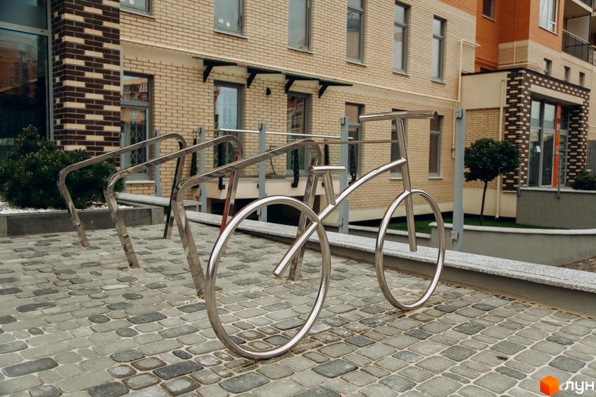 Фасад Житлового комплексу Водограй виконаний з бежевої цегли. Прибудинкова територія має бруківку та металеві велопарковки.