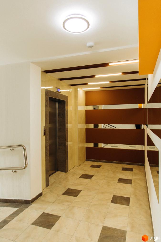 Інтер'єр вестибюлю Житлового комплексу Водограй з ліфтом, світлою плиткою на підлозі та дзеркальними стіновими панелями.