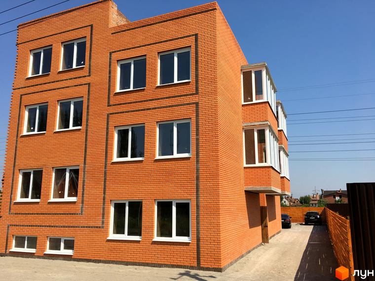 Житловий комплекс Затишний Хотів: цегляний будинок з білими вікнами та заскленими балконами. Перед будинком асфальтована дорога та парковка.