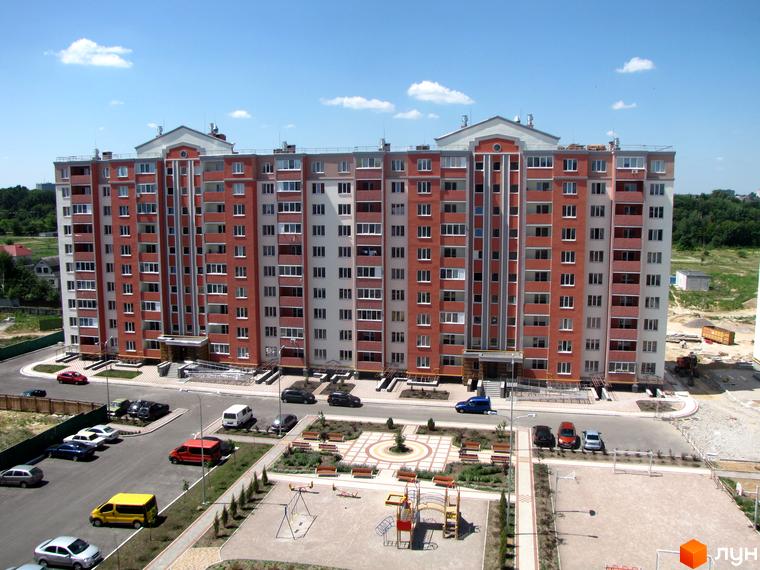 Житловий комплекс Квартал Тарасівський: багатоповерховий будинок з червоною цегляною облицовкою та білими вставками. На прибудинковій території розташовані паркувальні місця, дитячий майданчик та лавочки.