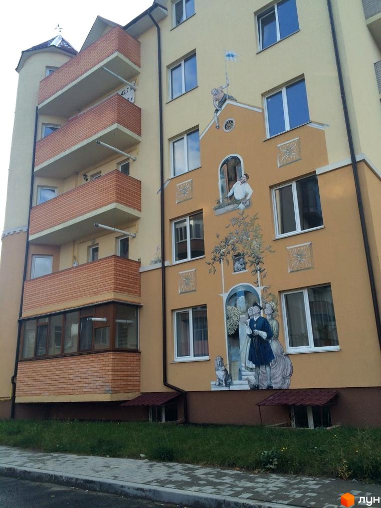 Зовнішній вигляд будинку ЖК Нагірний з балконами та муралами на фасаді. Прибудинкова територія з травою та тротуаром.