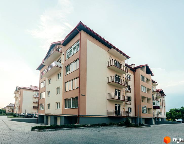 Житловий комплекс Вишневий сад. Багатоповерховий будинок з балконами та панорамними вікнами. На передньому плані викладена тротуарною плиткою прибудинкова територія.