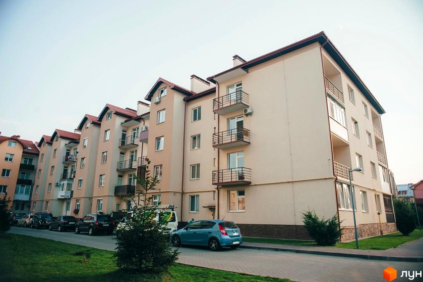 Житловий комплекс Вишневий сад. Багатоповерховий будинок з балконами та червоним дахом. На прибудинковій території є зелені насадження та припарковані автомобілі.