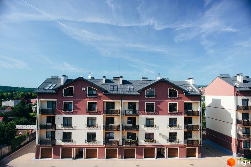 Зовнішній вигляд багатоповерхового будинку ЖК Едельвейс з червоною цегляною кладкою та світлими фасадами. На території комплексу є гаражі та балкони.