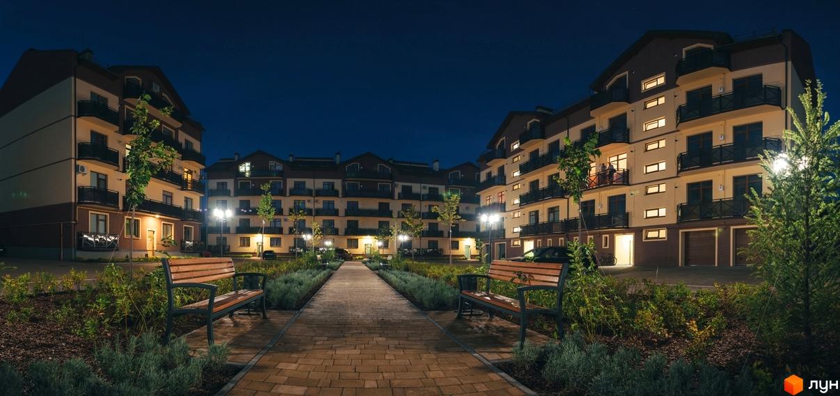Зображення житлового комплексу Едельвейс вночі. Багатоповерхові будинки з балконами та освітленням, доріжка з бруківки та лавки для відпочинку.