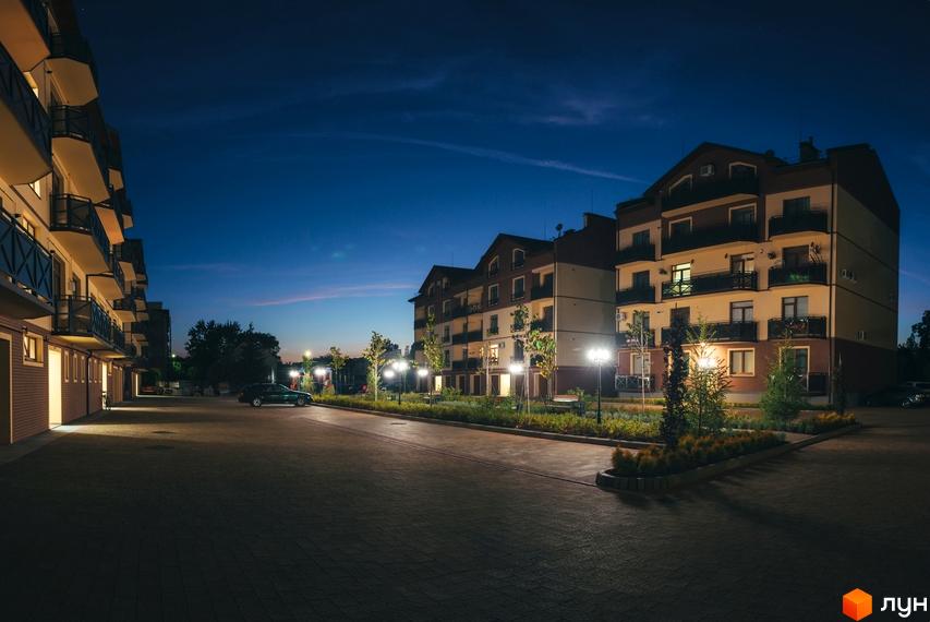 Житловий комплекс Едельвейс ввечері. Багатоквартирний будинок з балконами та терасами, освітлена прибудинкова територія з зеленими насадженнями та місцями для паркування.