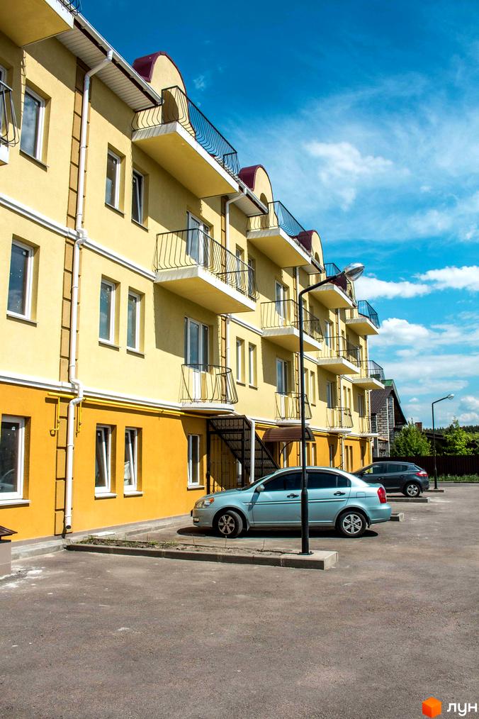 Житловий комплекс Вересковий. Жовтий триповерховий будинок з балконами та червоними дахами. На передньому плані припарковані автомобілі.