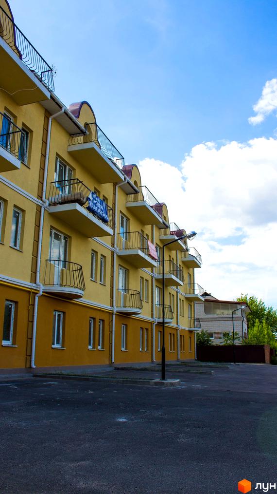 Житловий комплекс Вересковий з жовтими фасадами та балконами. На прибудинковій території асфальтована дорога та ліхтарі.