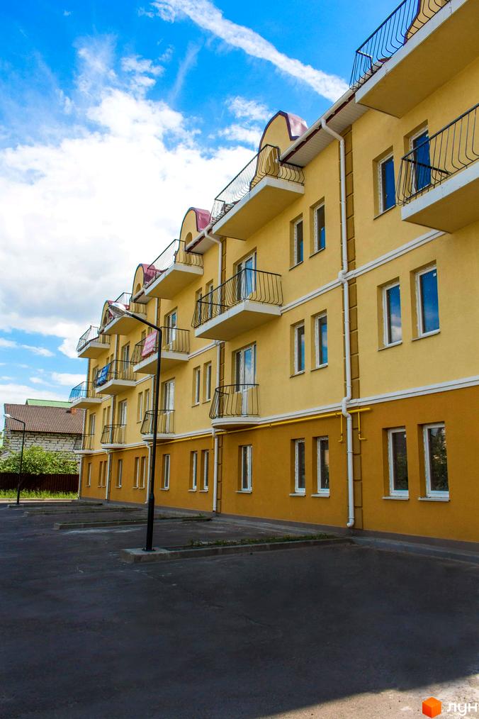 Житловий комплекс Вересковий з жовтим фасадом та балконами. На території комплексу асфальтована парковка, блакитне небо з хмарами.