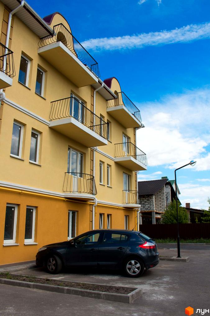 Житловий комплекс Вересковий з жовтим фасадом та балконами. На території комплексу є парковка для автомобілів та блакитне небо з хмарами.