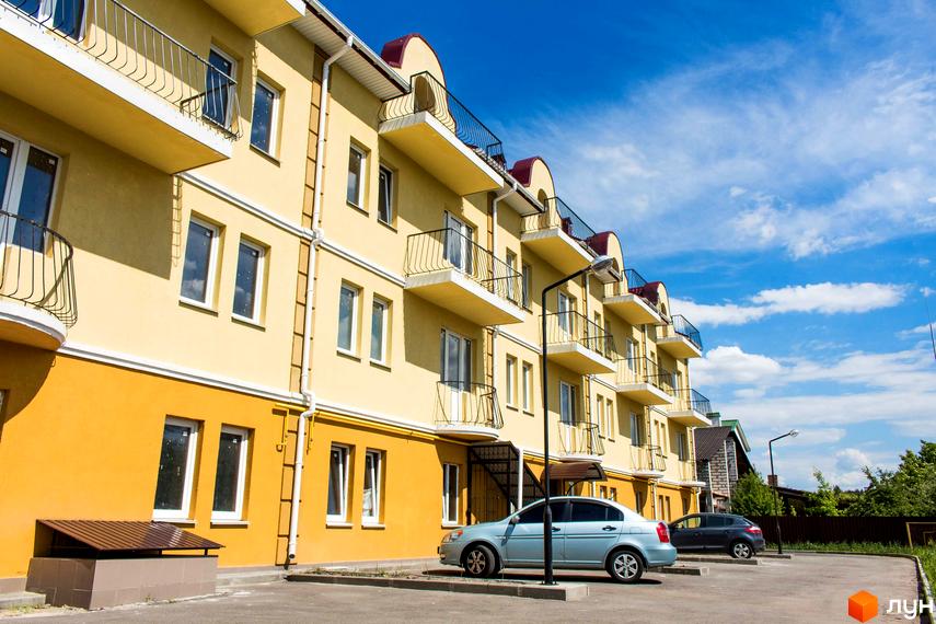 Зовнішній вигляд будинку ЖК Вересковий з балконами та паркуванням. Житловий комплекс розташований на сонячній стороні, з блакитним небом на задньому плані.