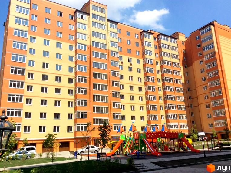 Багатоповерховий будинок з фасадом з цегли. На прибудинковій території розташований дитячий майданчик та зелені насадження.