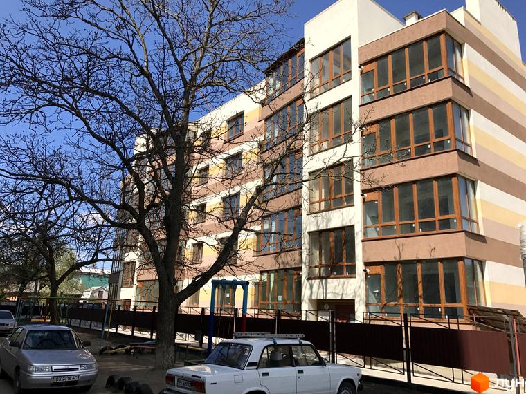 Новобудова Будинок мрії має багатоповерховий фасад зі смугами різних кольорів та великими вікнами. Перед будинком видно дерева та дитячий майданчик.