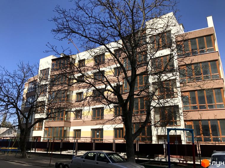 Багатоповерховий будинок ЖК Будинок мрії з панорамними вікнами. На передньому плані видно дерева та прибудинкову територію.