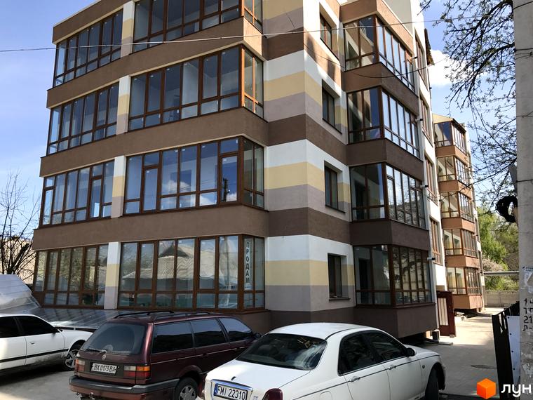 Житловий комплекс Будинок мрії – багатоповерхова новобудова з великими вікнами та балконами. Навколо будинку розташовані автомобілі та дерева.