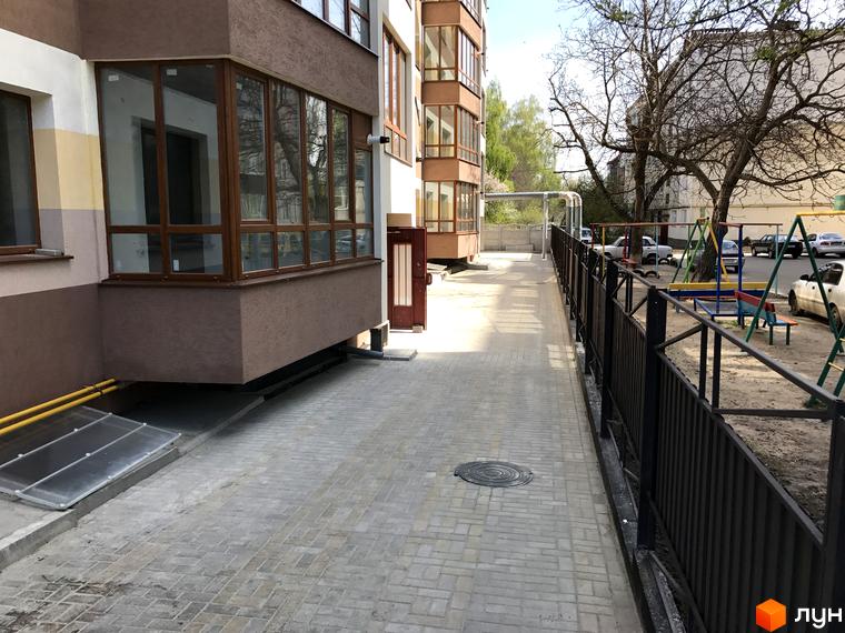 Житловий комплекс Будинок мрії з коричневими вікнами та фасадом. Поруч дитячий майданчик та парковка.