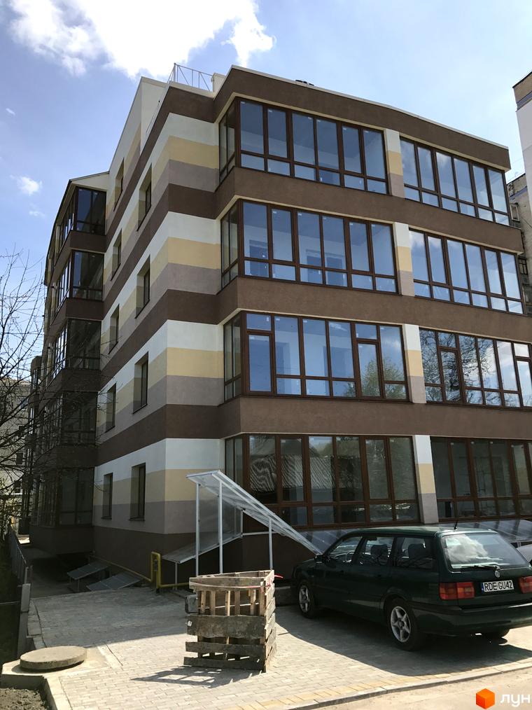 Житловий комплекс Будинок мрії має багатоповерховий будинок з фасадом у кольорові смуги та великими вікнами. Біля будинку розташована бруківка та автомобіль.