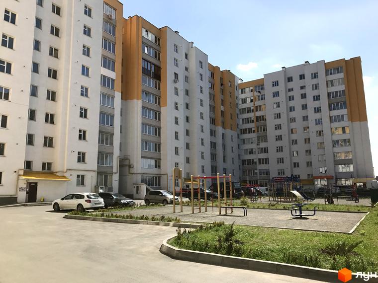 Зовнішній вигляд багатоповерхових будинків житлового комплексу на вул. Зарічанська, 9. Прибудинкова територія з дитячим майданчиком та парковкою.