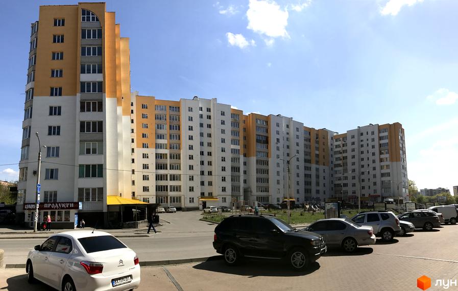 Новобудова на вулиці Зарічанська, 9. Багатоповерховий будинок з жовто-білим фасадом та прибудинковою територією з автомобілями.