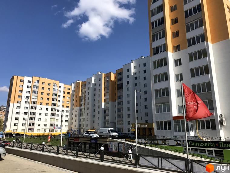 Житловий комплекс на вулиці Зарічанська, 9. Багатоповерхові будинки з білими та помаранчевими фасадами, вікна з темними рамами, парковка.