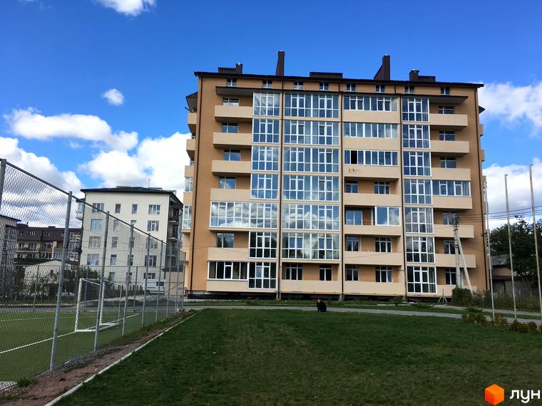 Зображення фасаду та прибудинкової території Житлового комплексу Європейський квартал. Багатоповерховий будинок з великими вікнами та газоном.