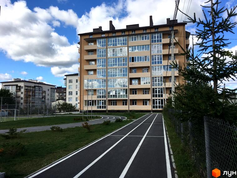 Зображення житлового комплексу Європейський квартал. Багатоповерховий будинок з великими вікнами та балконами, поруч бігова доріжка та зелена територія.