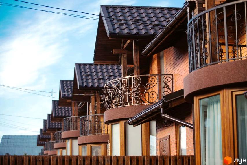 Котеджне містечко Sun House: фасади з цегли та темні черепичні дахи з кованими балконами. Поруч дерев'яний паркан.