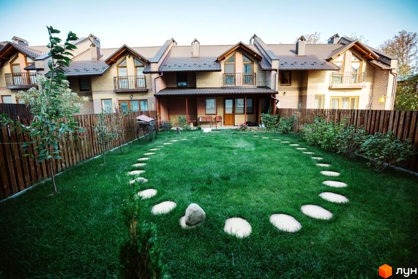 Котеджне містечко КМ Sun House з цегляними фасадами та коричневими дахами. На прибудинковій території доглянутий газон, дерев'яна огорожа та доріжка з каменів.