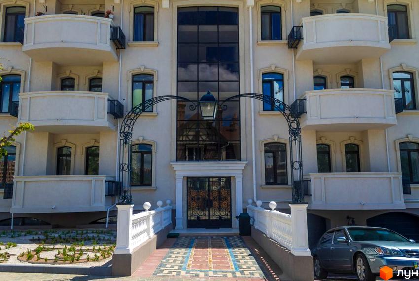 Житловий комплекс Palais Royal: елегантний фасад з балконами та аркою з ліхтарем. Прибудинкова територія з доглянутими клумбами та дорогою.