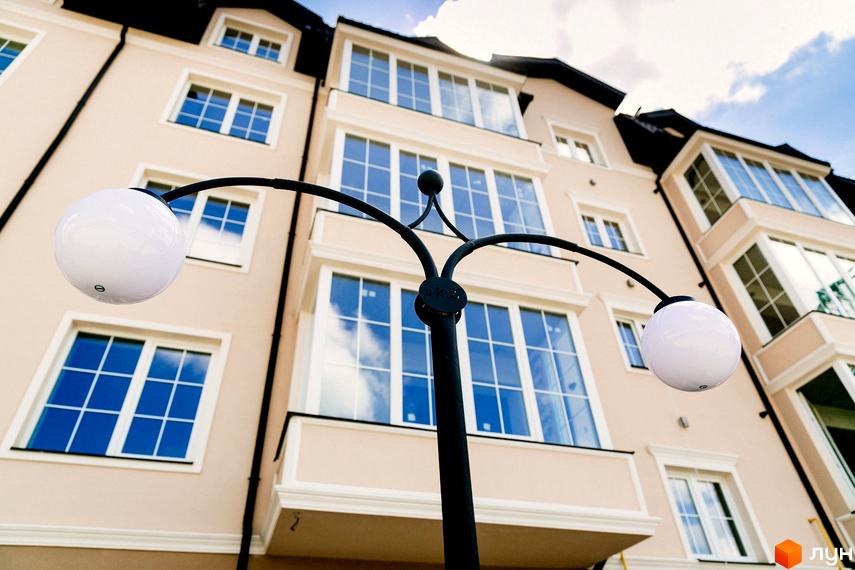 Житловий комплекс Маєток Боздош. Фасад будинку з великими вікнами та світлодіодними ліхтарями. Небо з хмарами відбивається у вікнах.