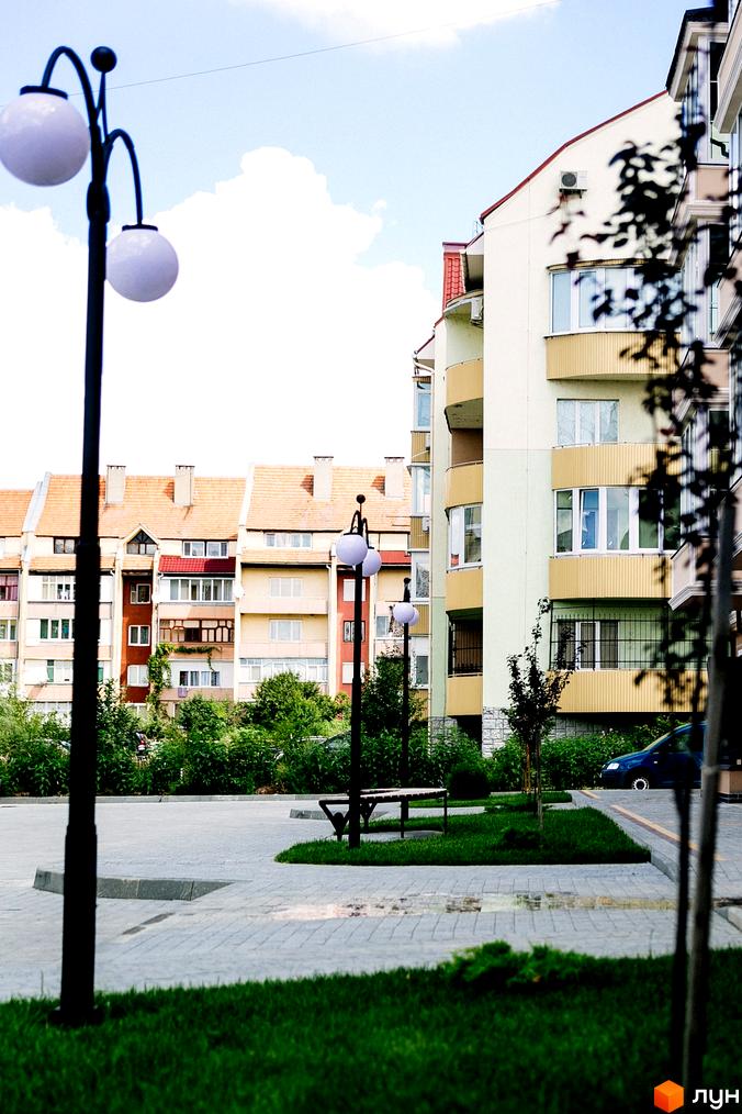 Зображення фасаду житлового будинку ЖК Маєток Боздош з балконами та вікнами. На передньому плані – вуличні ліхтарі та зелена прибудинкова територія з газоном.