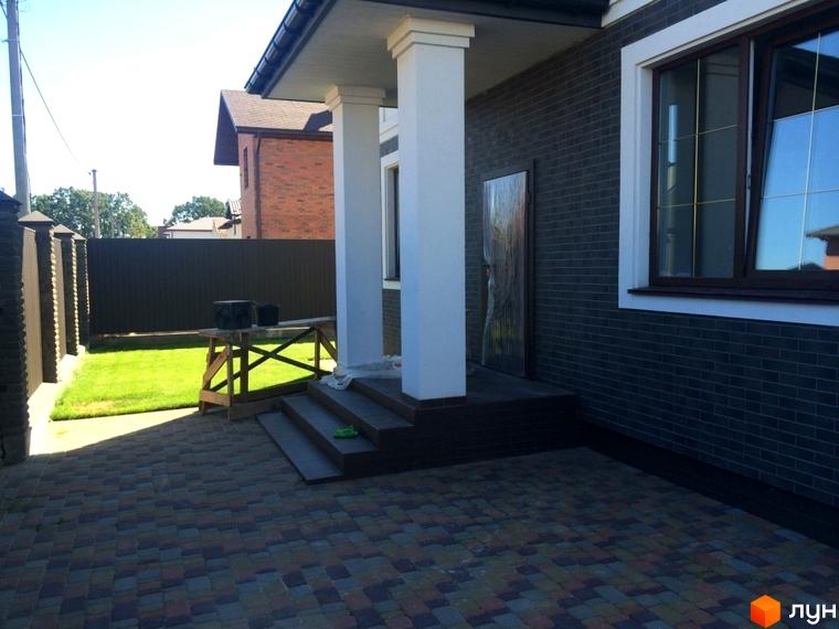 Зображення фасаду будинку в Котеджному містечку Петропавлівський Luxe з темною цегляною кладкою. На передньому плані вимощена бруківкою прибудинкова територія та сходи до будинку.