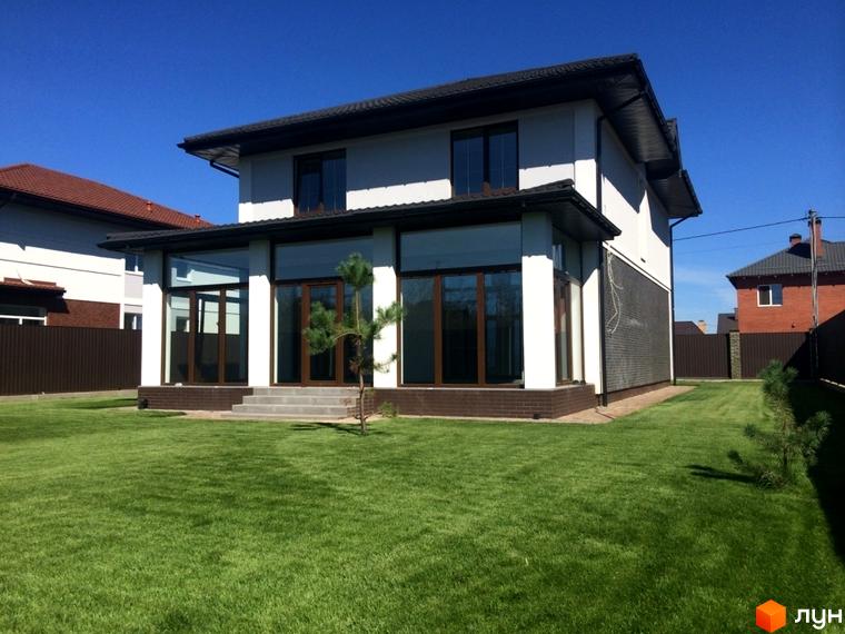 Двоповерховий будинок Котеджного містечка Петропавлівський Luxe з білими стінами, темним дахом та панорамними вікнами. Навколо доглянутий зелений газон.